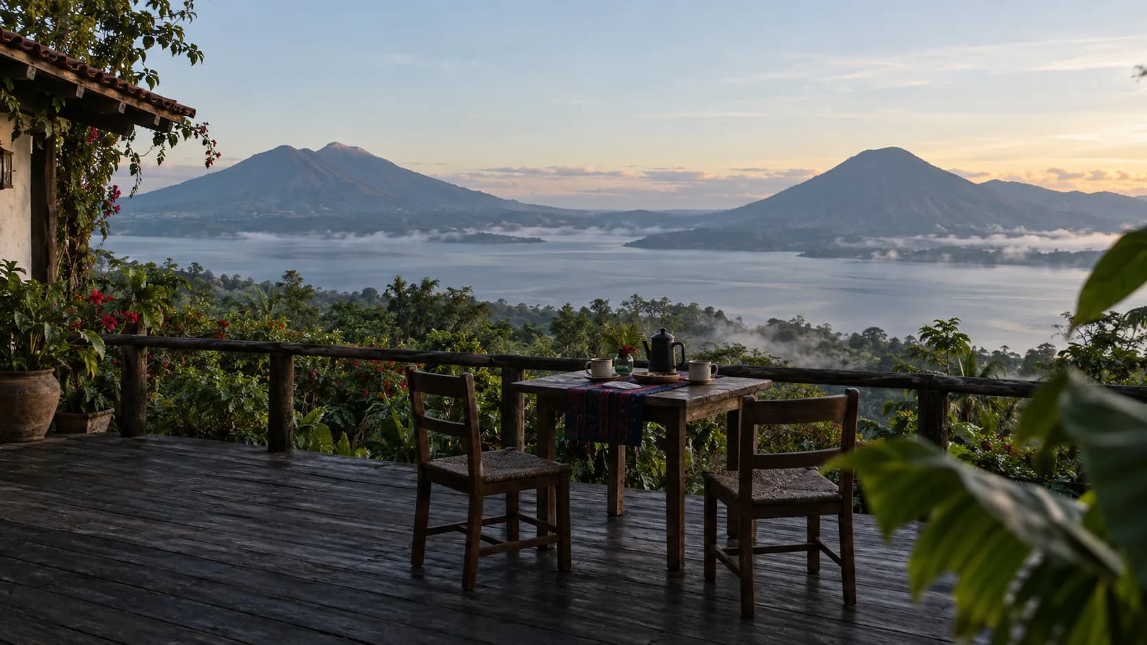 A timber terrace at a small lodge at first light, a table set for two, looking across a highland lake to volcanoes in haze.